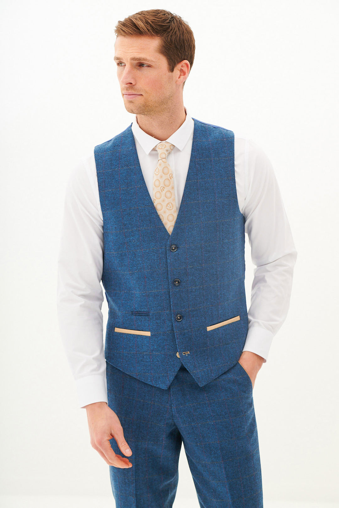 A man models the marcdarcy DION Blue Tweed Check Three Piece Suit with matching trousers, white shirt, and beige patterned tie, standing against a plain white background and looking slightly to the side.