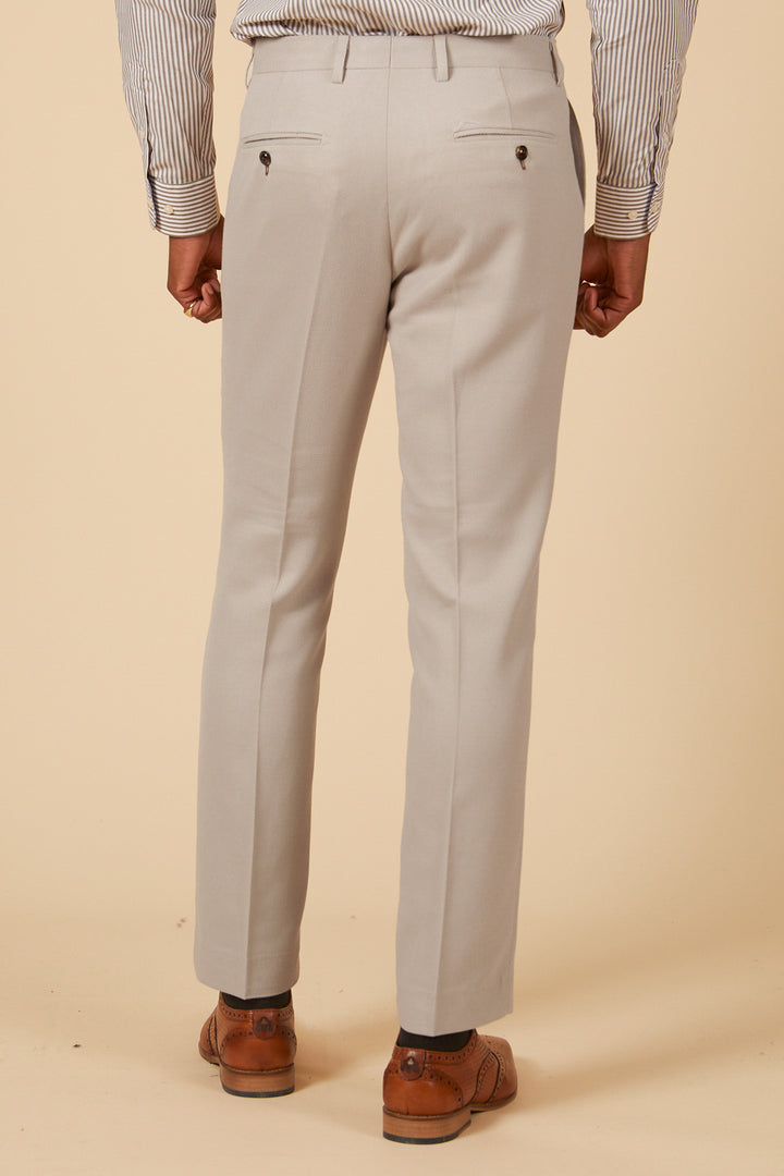 A person models the Marc Darcy HM5 - Stone Tailored Three Piece Suit, shown from behind against a plain beige background, highlighting its slim-fit silhouette.