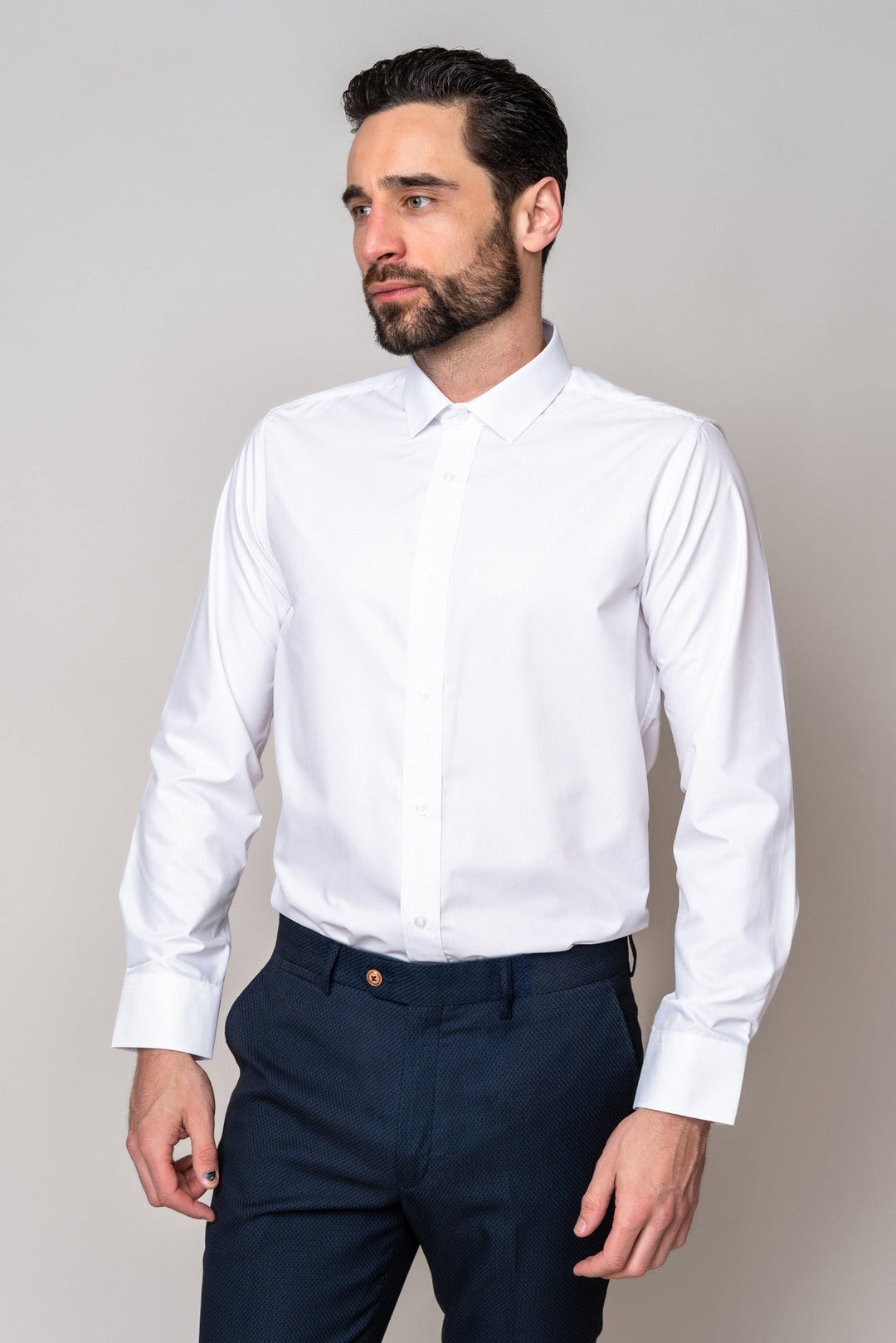 A man with dark hair and a beard wears the Marc Darcy CARTER white long sleeve shirt in a classic fit with a spread collar, paired with dark trousers, standing against a light background and looking slightly left.